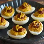 deviled eggs with hotdogs and mustard on them sitting on a black tray