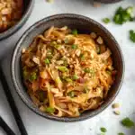 a white bowl filled with noodles and topped with green onions next to chopsticks