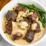 a white plate topped with meat covered in gravy and garnished with parsley