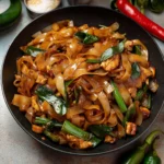 two pictures of stir fry noodles with chicken, peppers and green onions in a skillet