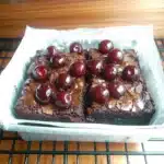 chocolate cherry brownies on parchment paper with cherries in the background and text overlay