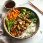 two bowls filled with rice, chicken and broccoli covered in teriyaki sauce
