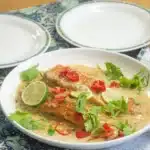grilled salmon with sauce and garnishes on a white plate next to a lime wedge