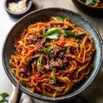 a bowl filled with noodles and meat on top of a white tablecloth next to chopsticks
