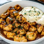 chicken bites with garlic sauce being drizzled over them on top of a plate