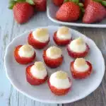 A plate of strawberry cheesecake cups topped with white chocolate drizzle and garnished with fresh strawberries, perfect for springtime indulgence. These quick and easy cups bring together a creamy cheesecake filling, fresh fruit, and a graham cracke...