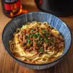 a bowl of noodles with meat and green onions