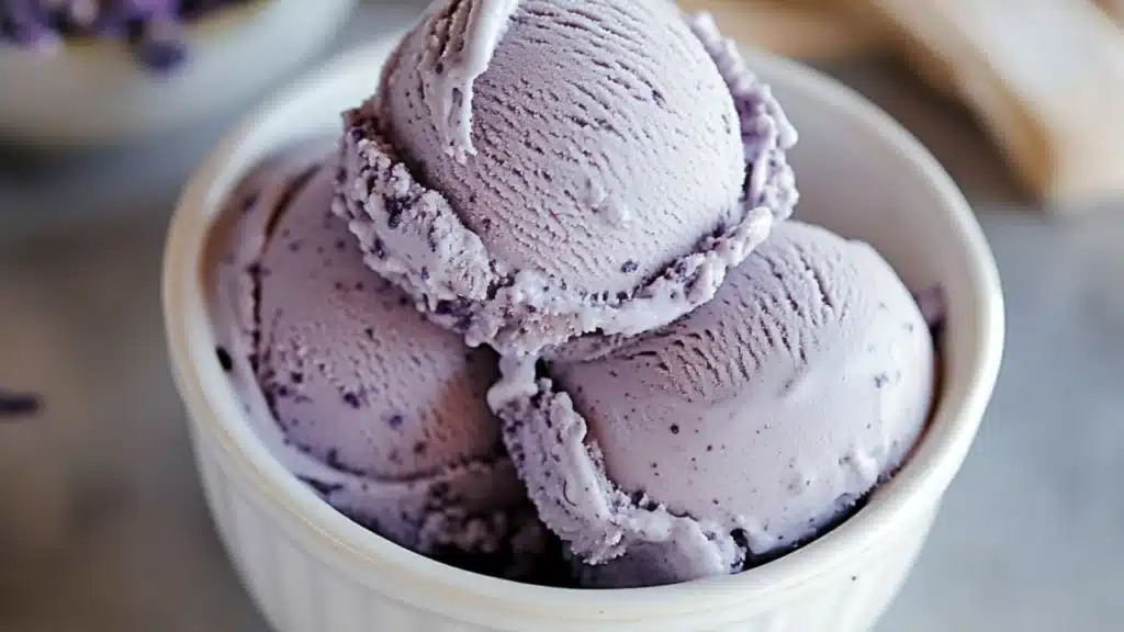 lavender ice cream in a white bowl with green leaves on top and the words lavender ice cream